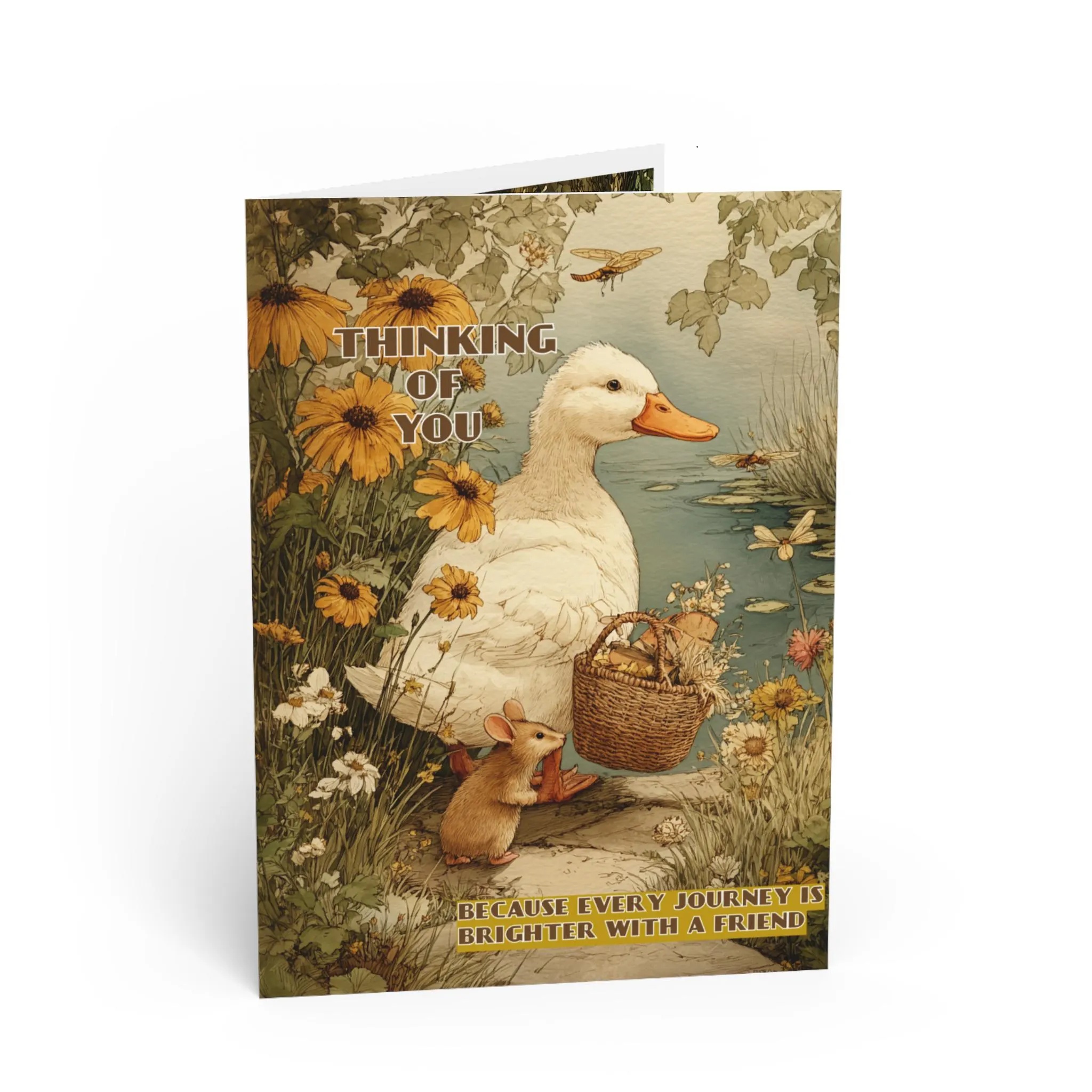 Mockup of a premium folded greeting card featuring a white duck carrying a picnic basket alongside a small mouse by a peaceful pond with blooming wildflowers and dragonflies. The front reads 'Thinking of You' with the heartfelt message, 'Because Every Journey Is Brighter With a Friend.'